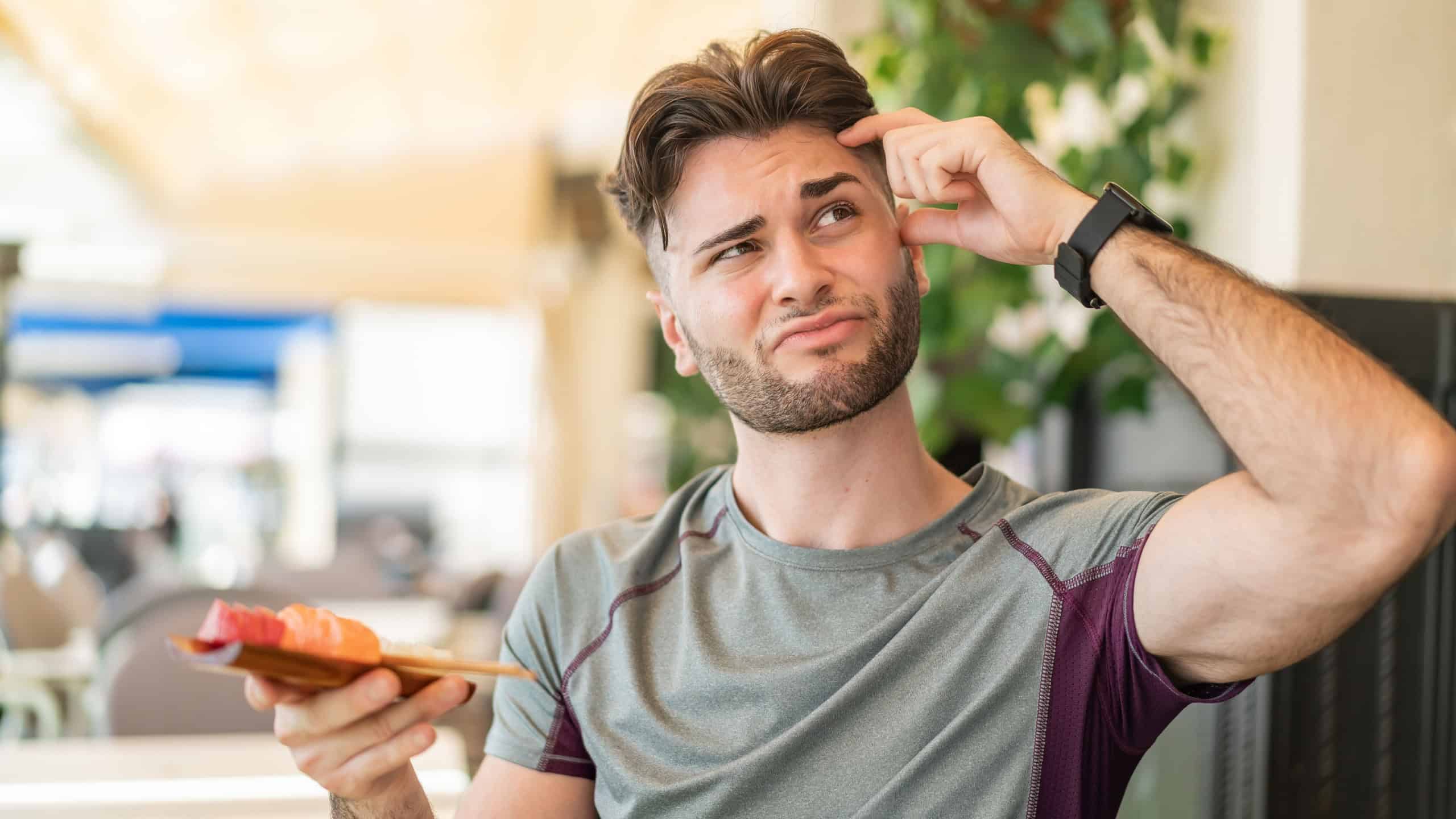 Young handsome man holding sashimi at outdoors having doubts and with confuse face expression