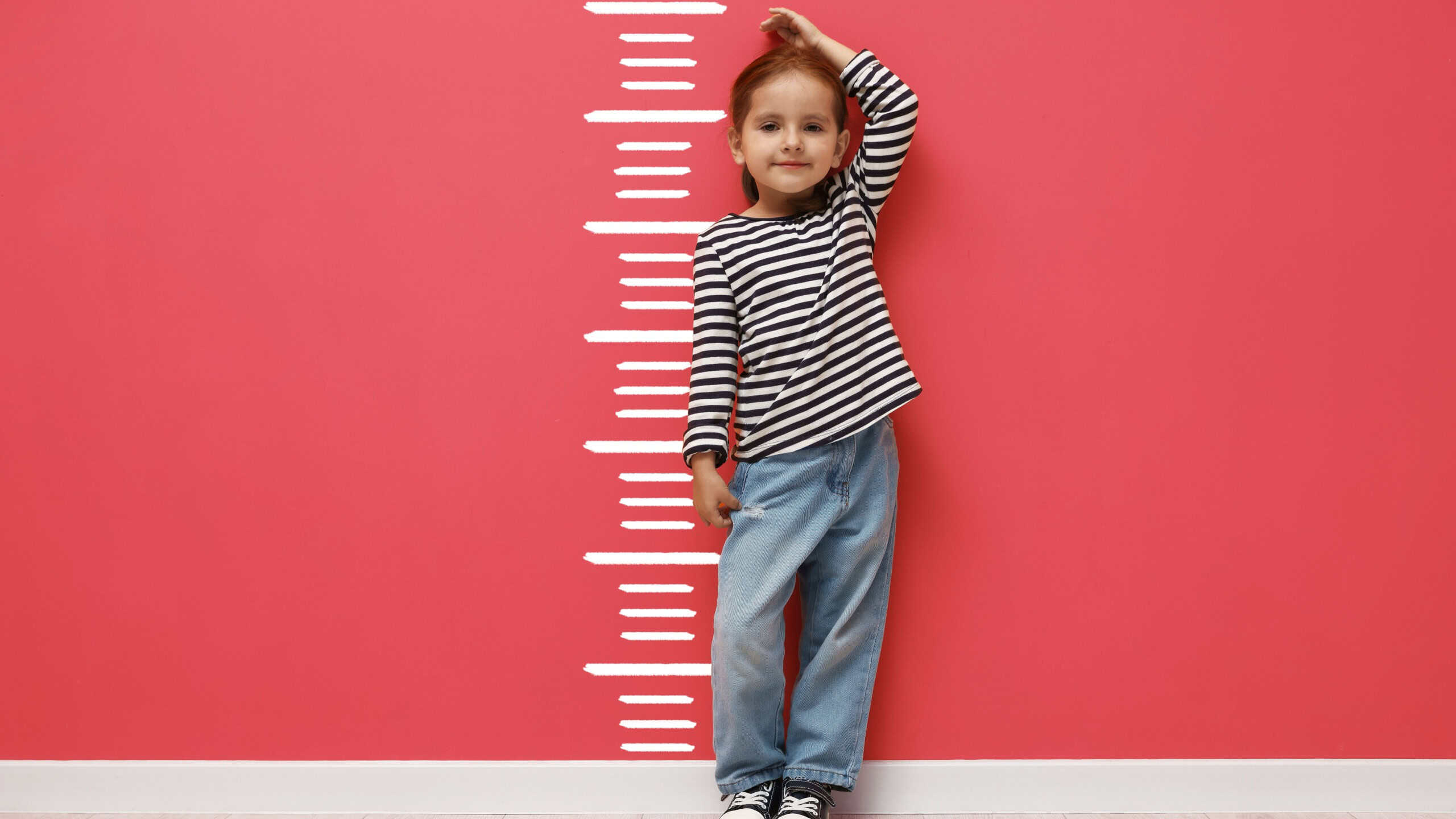 Cute little girl measuring her height near coral color wall with scale