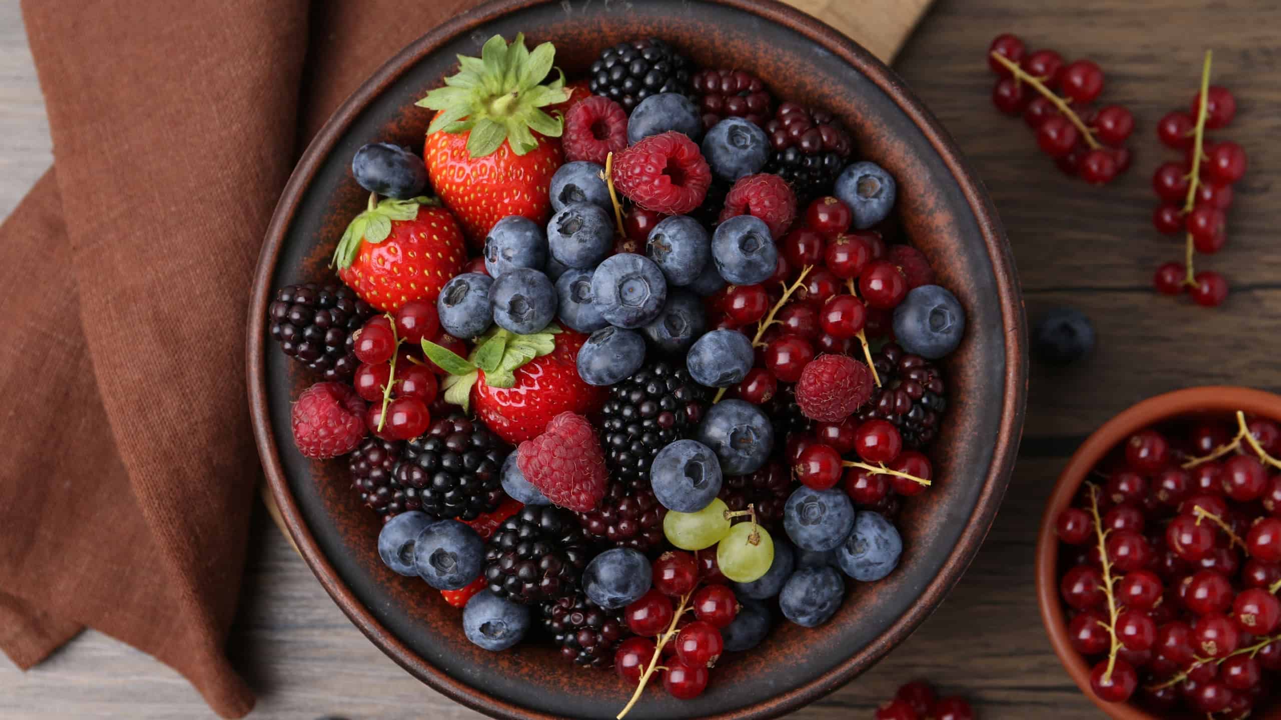 Different ripe berries in bowls on wooden table, flat lay