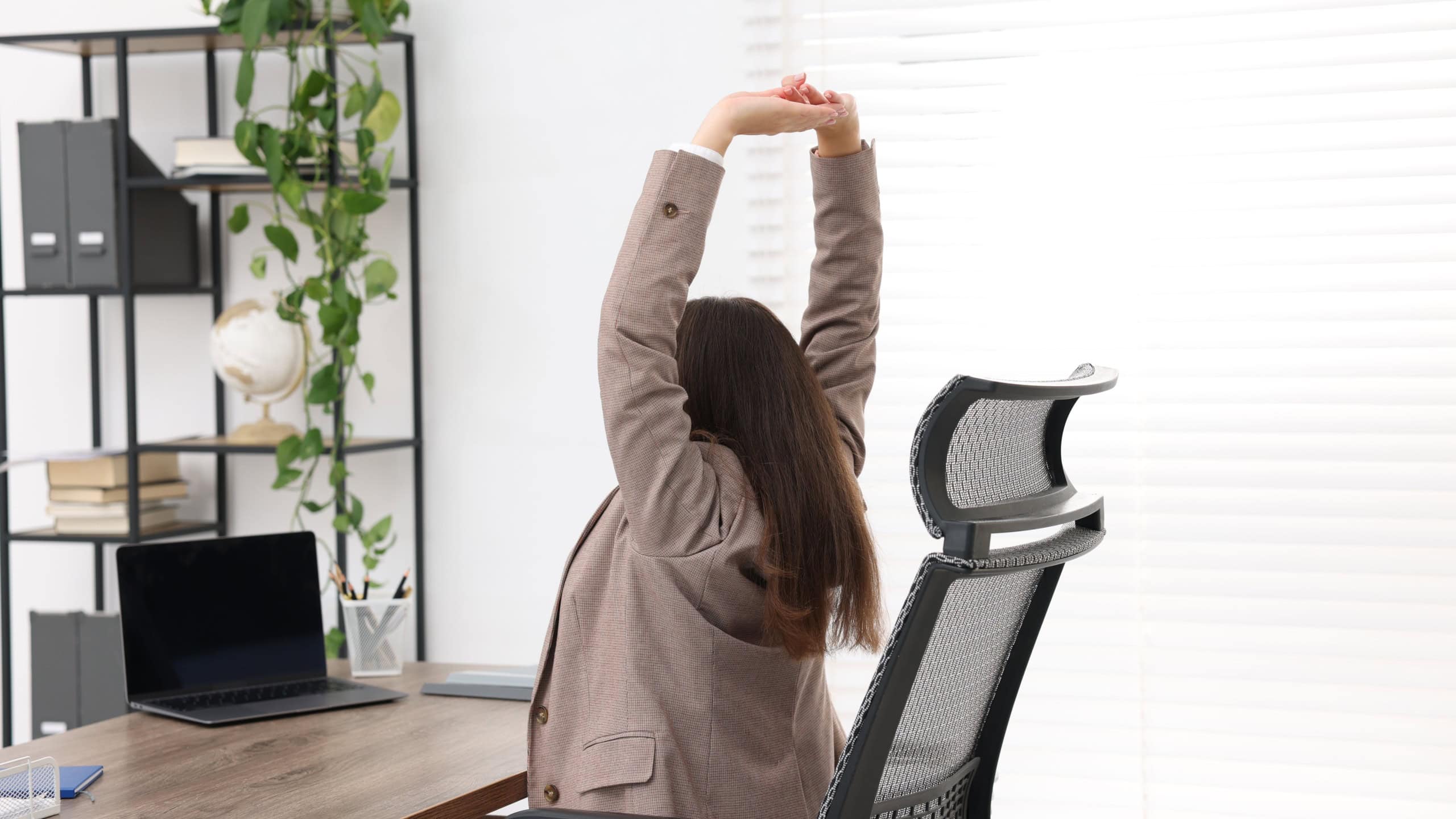 Young businesswoman stretching at table in office, back view