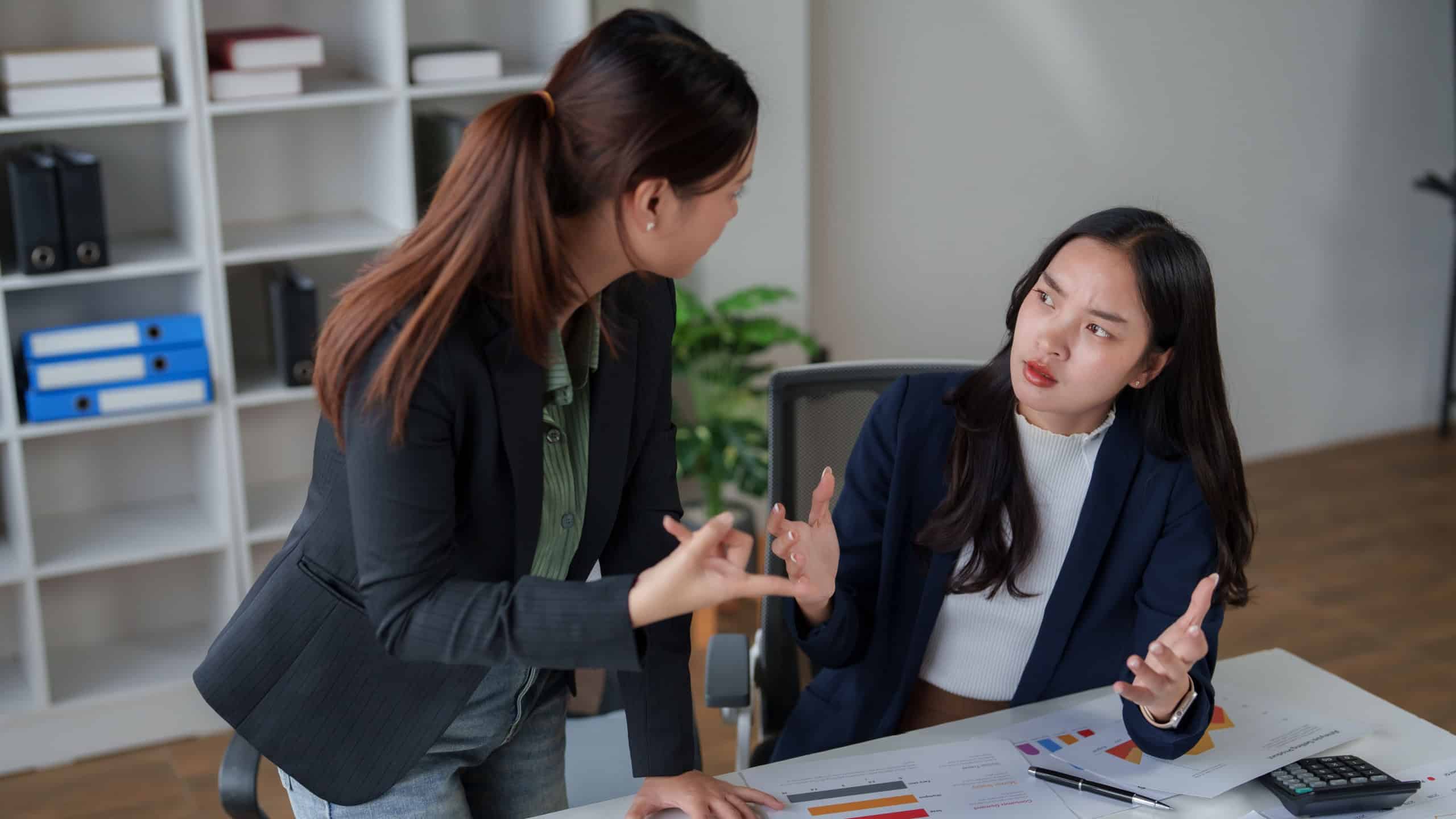 Two asian businesswomen in office discussing an argument, problem, or conflict at work. They are having a serious, tense conversation