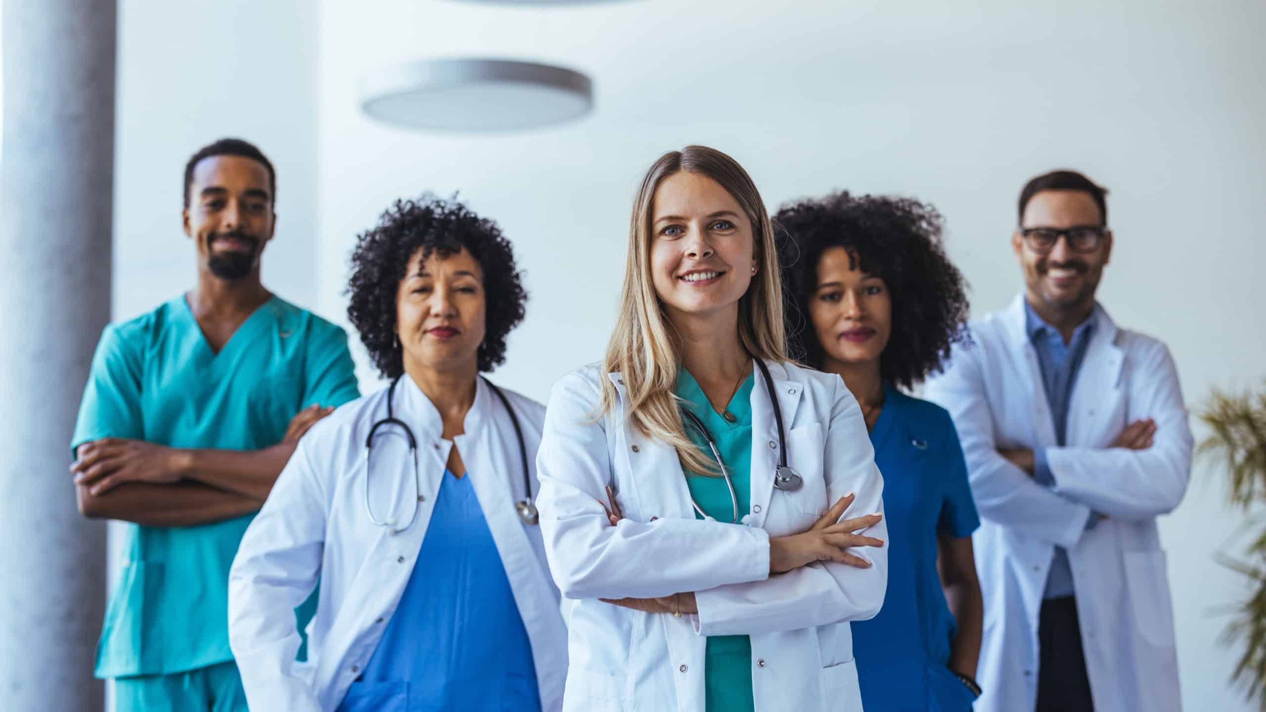 A diverse group of healthcare professionals, including doctors and nurses, stand confidently with arms crossed in a modern clinic environment. They symbolize teamwork, leadership, and patient care