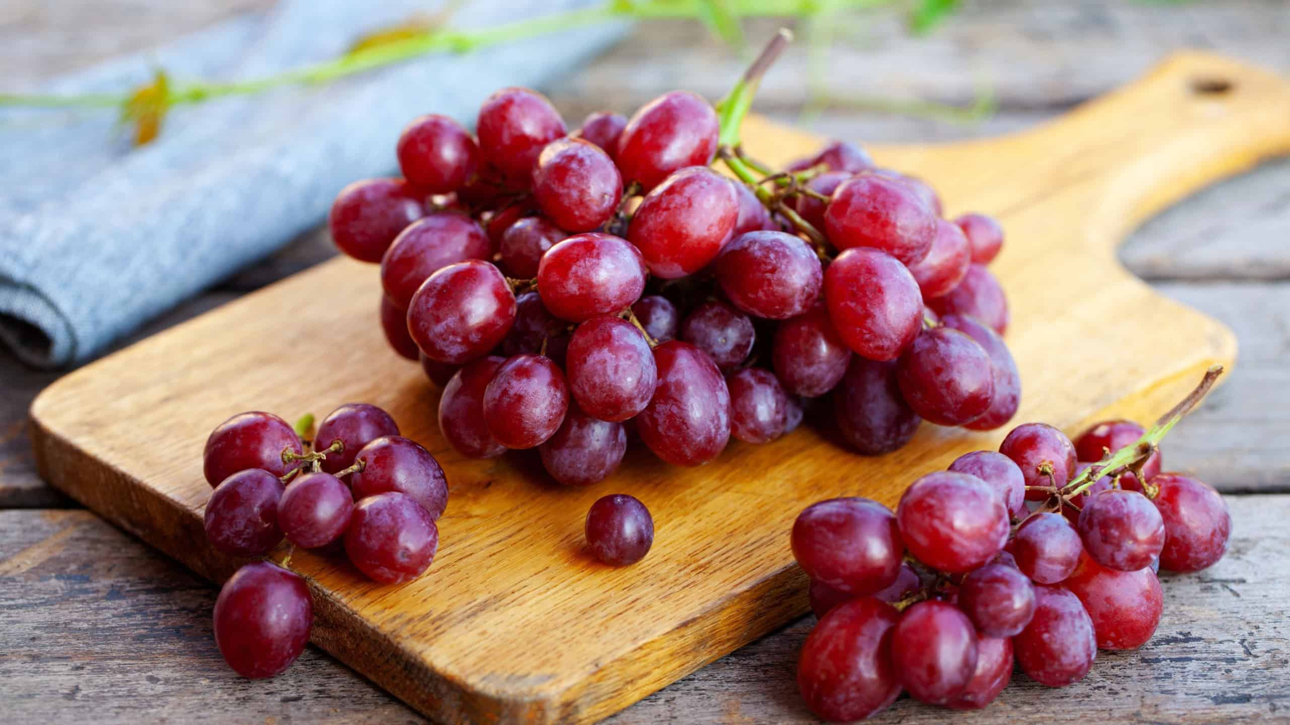 Fresh red grapes cluster on cutting board. Rustic wooden background. Close up.