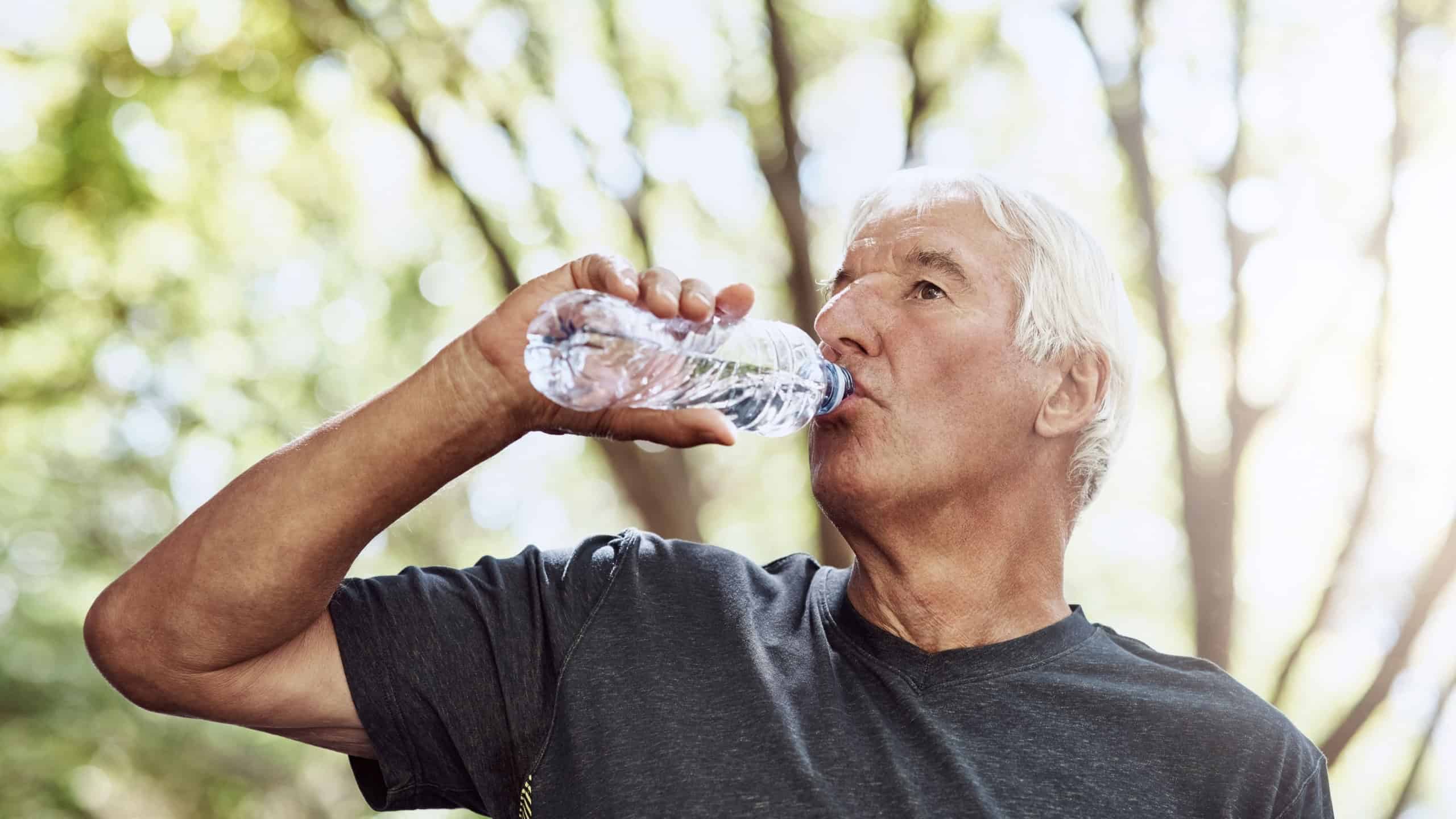 Senior man, drinking water and fitness at park with break, hydration and cardio challenge in summer. Elderly person, bottle or rest with liquid for electrolytes, wellness and exercise in retirement