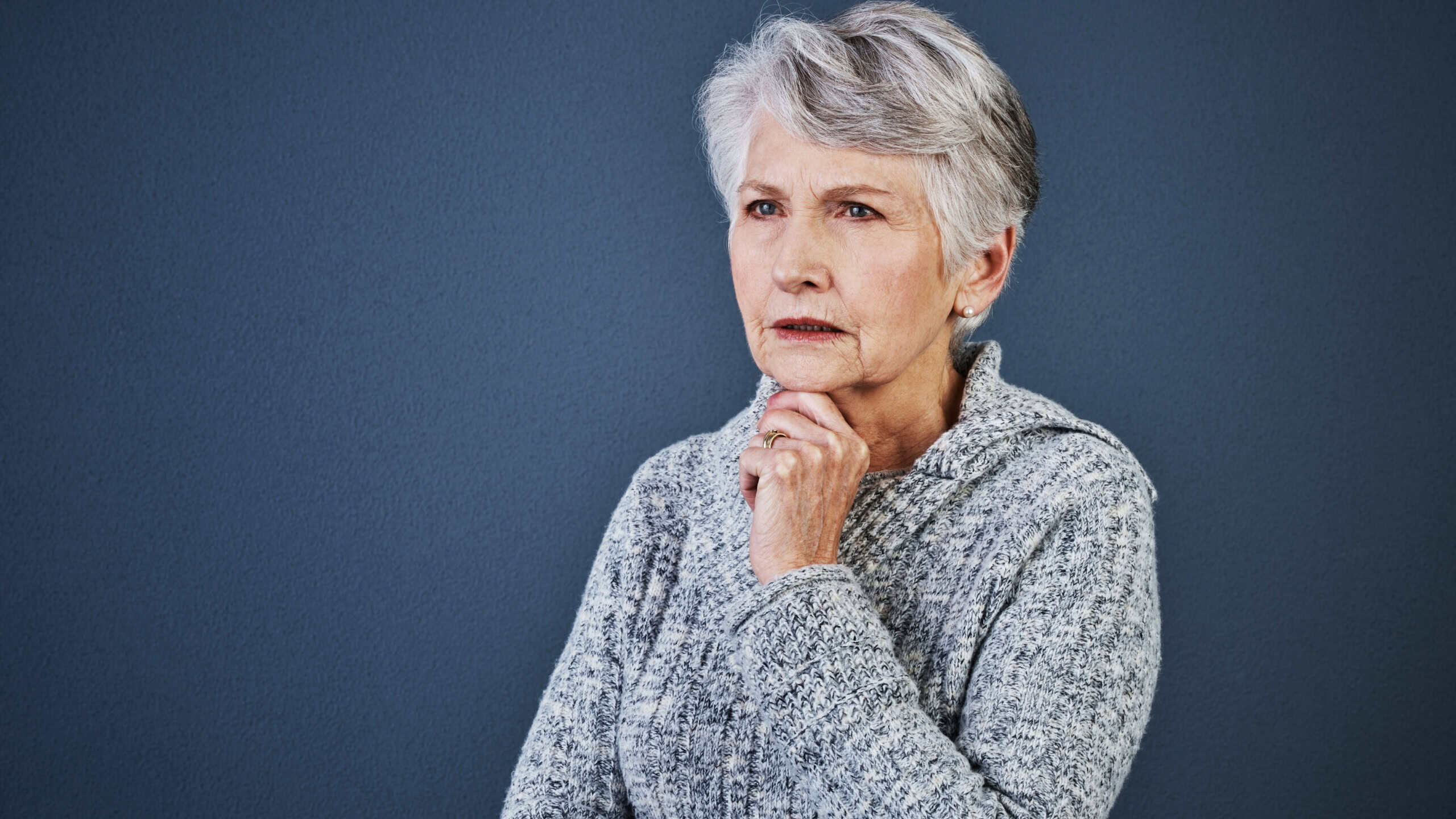 Elderly woman, thinking and reflection of question in studio for planning, idea and space. Senior person, mockup and brainstorming for decision, retirement and problem solving on gray background