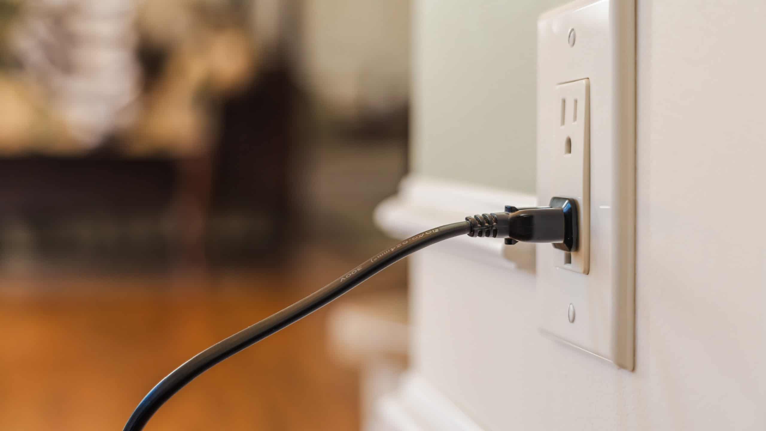 Power cable plugged into American wall outlet in modern home interior, close up of electrical socket and cord with soft blurred background. High quality photo