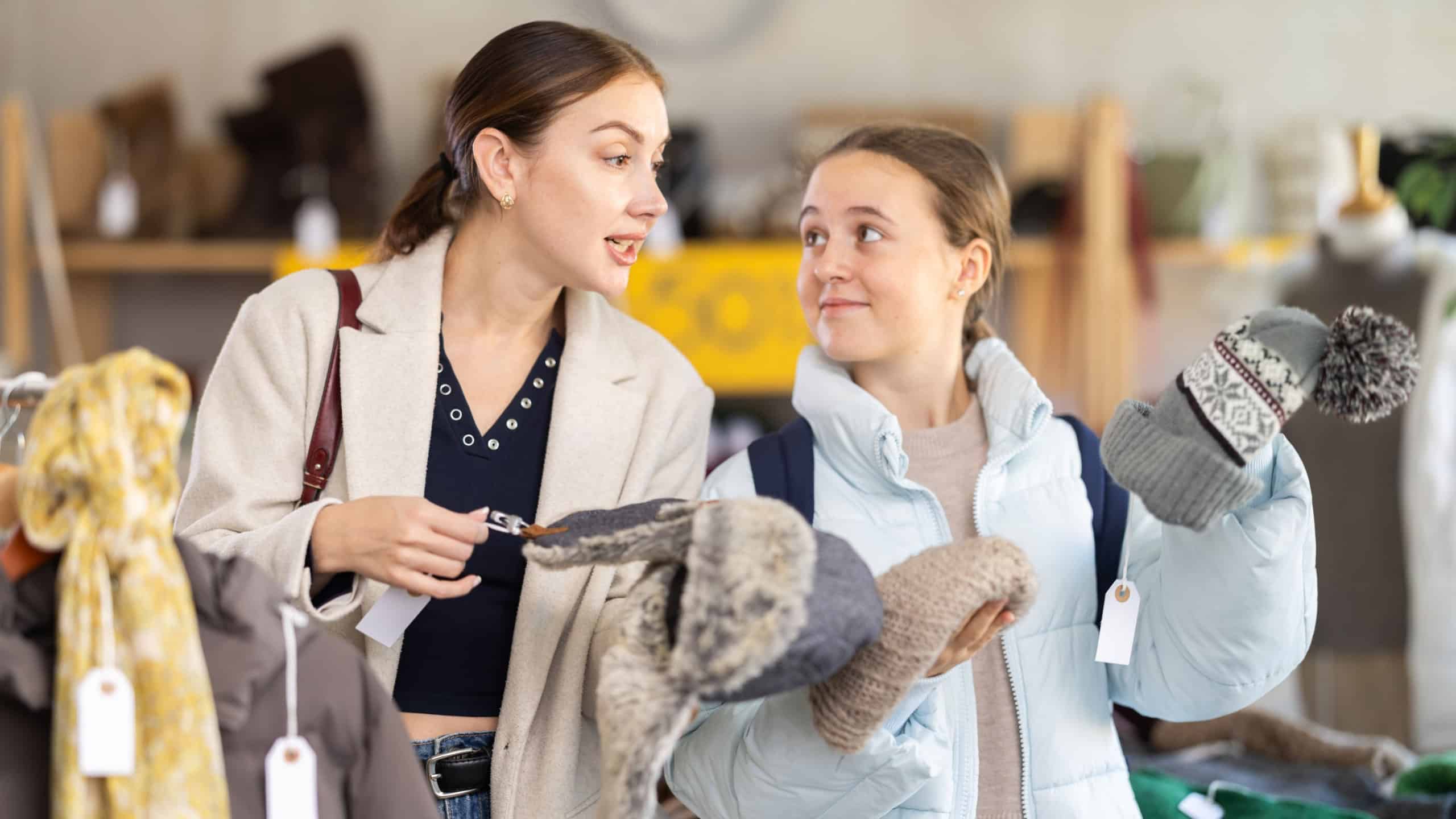 Glad mom and teenage daughter choosing winter hat during winter sale in clothing shop