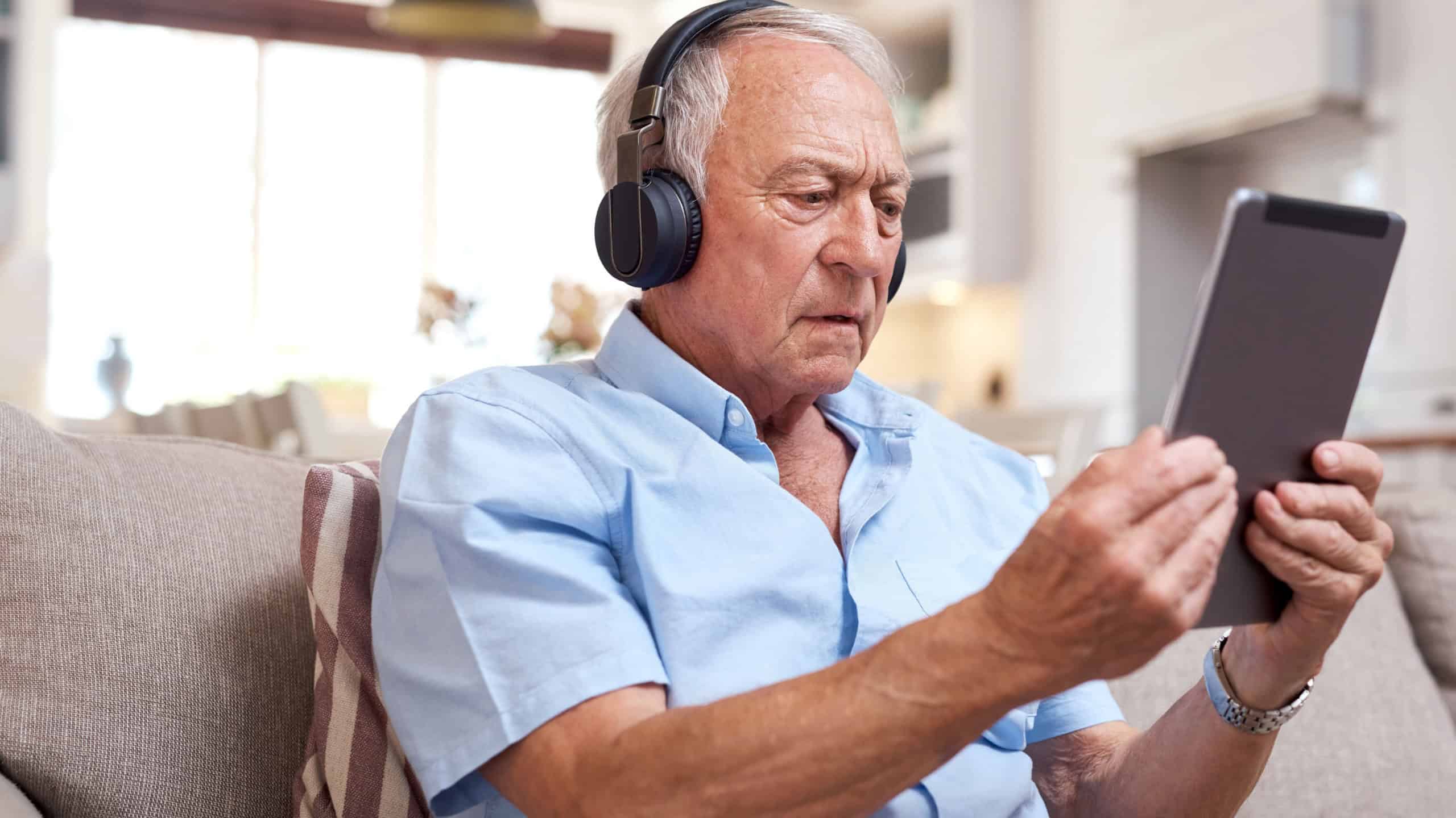 Headphones, old man or confused with tablet on sofa for connection fail, 404 error or technical issue. Streaming, senior person or tech stress in home for low battery, network glitch or slow internet