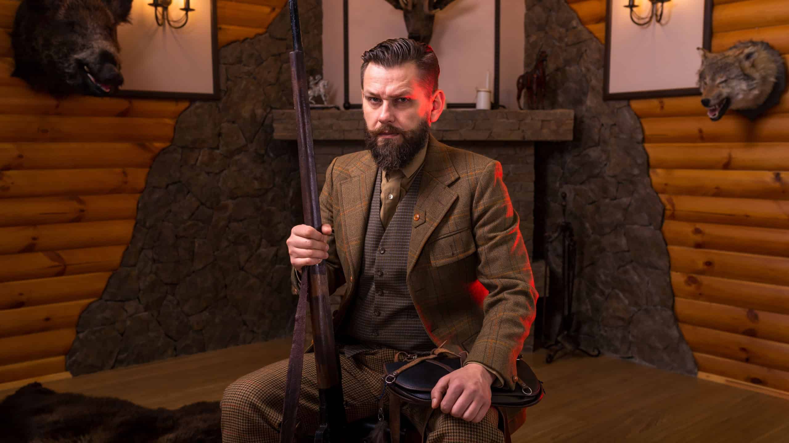 Hunter in traditional tweed clothing sitting and holding his rifle vertically