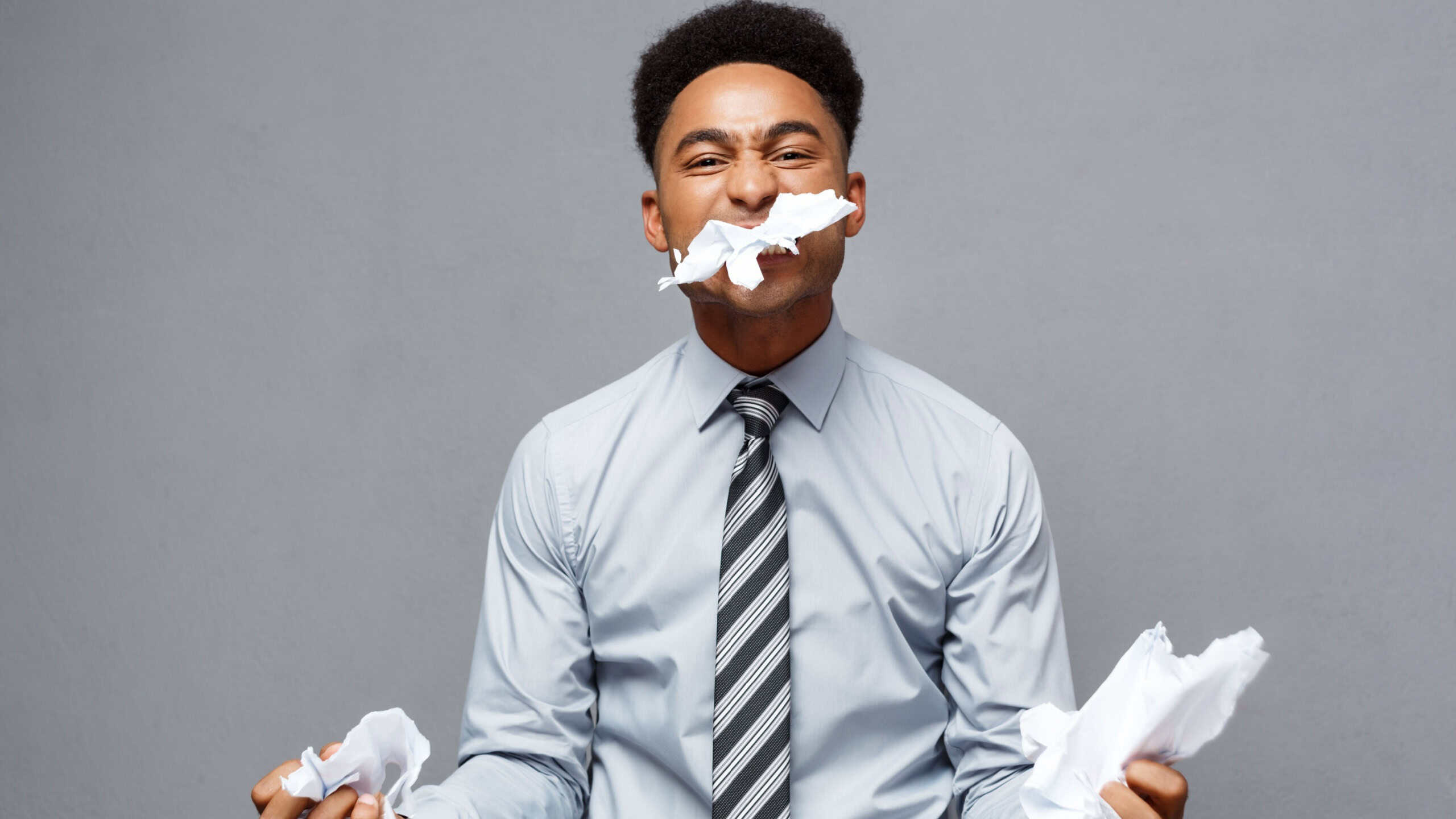 Business Concept - Young angry African American businessman while eating balled report paper. Unsuccessful Project.