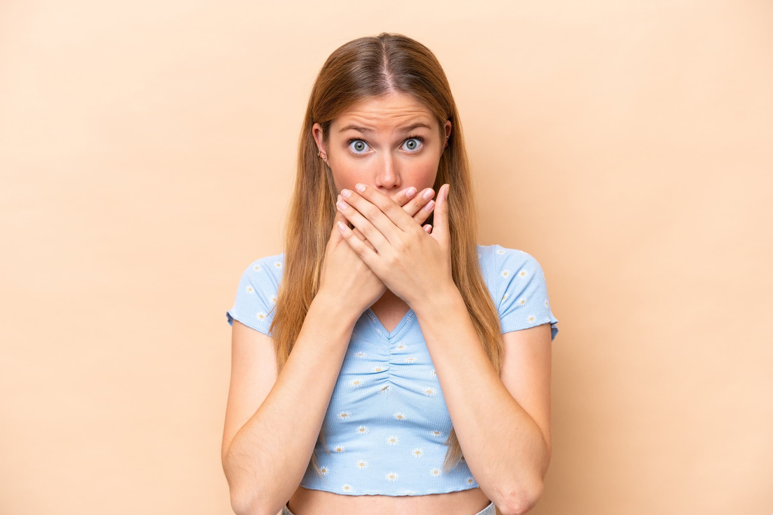 Young caucasian woman isolated on beige background covering mouth with hands
