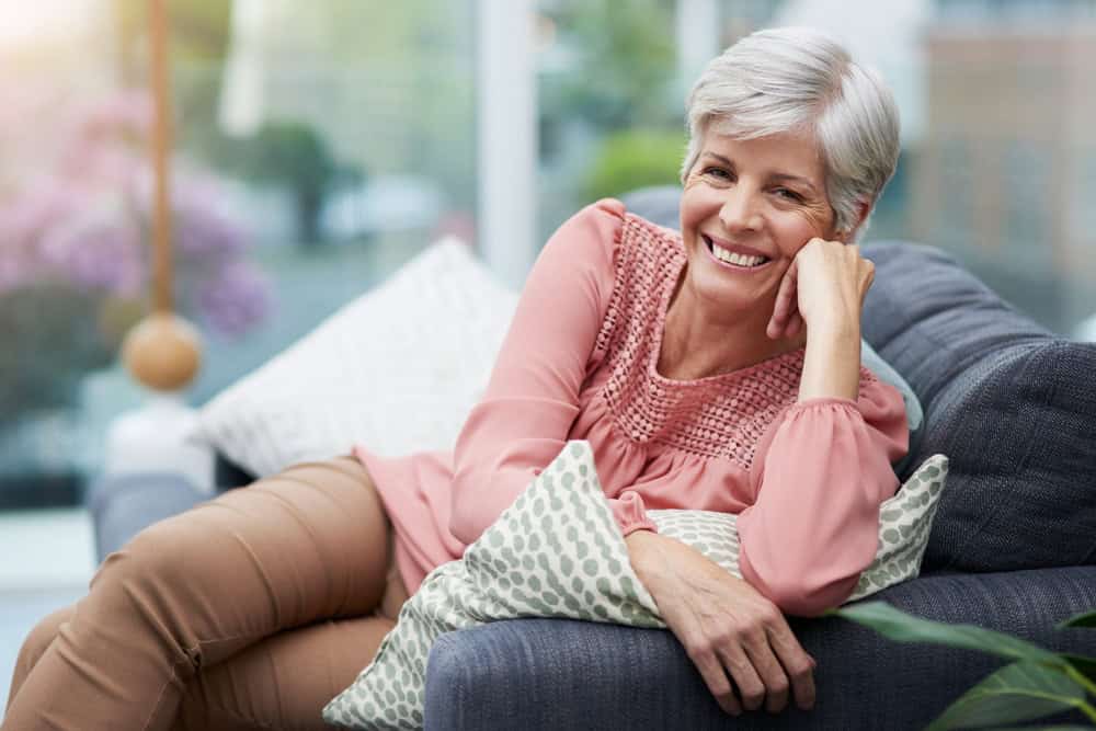 Portrait, house and senior woman on sofa, relax and happiness with retirement in living room. Face, pensioner and elderly lady with break, comfortable on couch or resting with peace, calming or smile