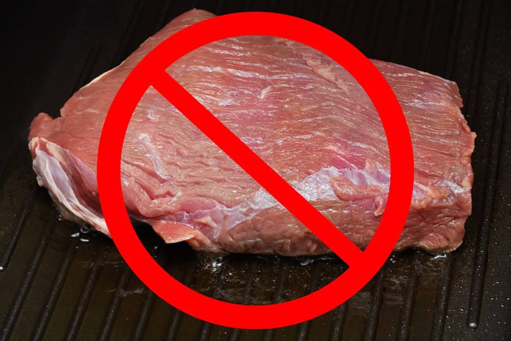 Healthy nutrition, diet and vegetarianism. Red prohibitory sign on a piece of meat, fried in a pan