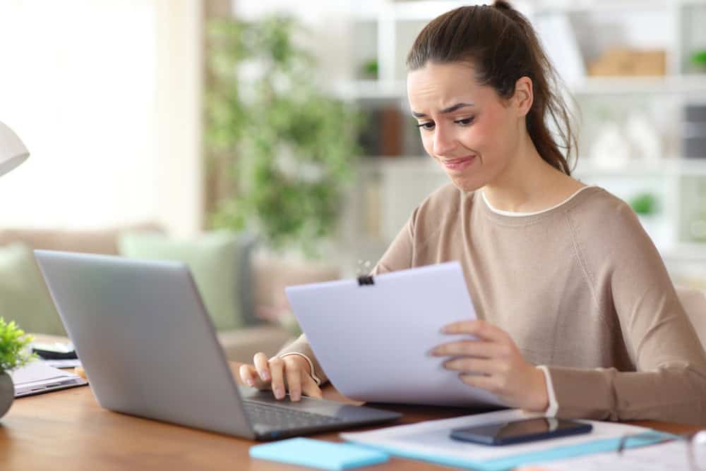 Worried freelance worker reading paper documents working online at home