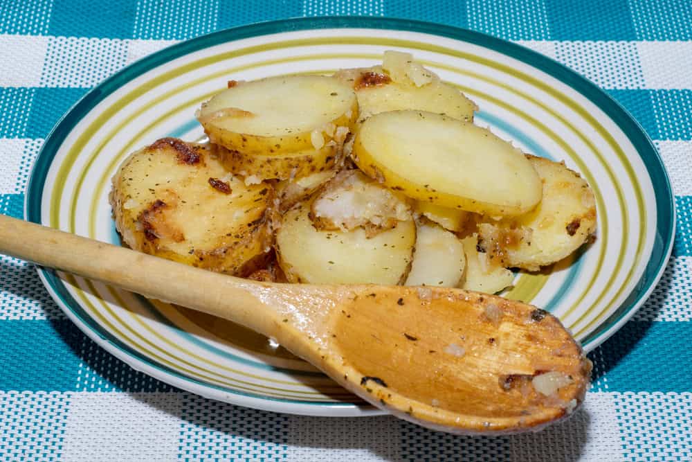 Hot baked potato slices with thin skinned potatoes on a plate with a wooden spoon. A simple and quick after-work meal for the worker and bachelor. Inexpensive food for poor people and farmers