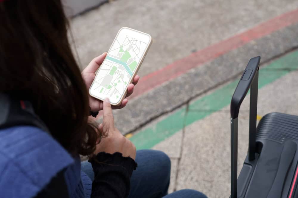 Woman with baggage in downtown city street searching location in map application online on smart phone using GPS navigating